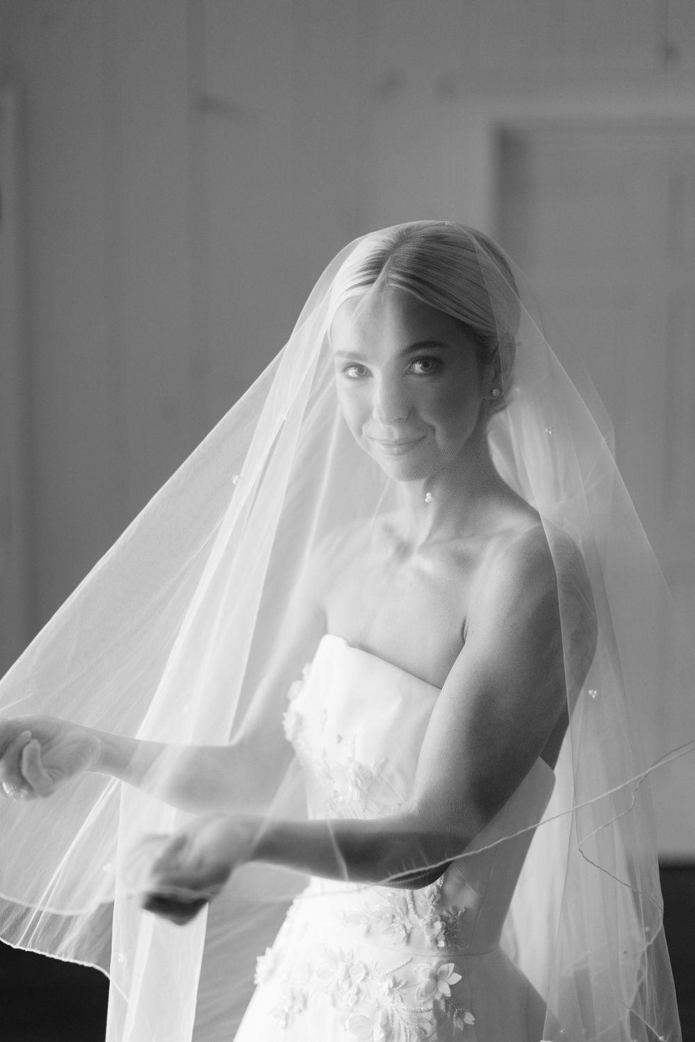Black and white portrait of a bride in a strapless wedding dress and flowing cathedral veil.