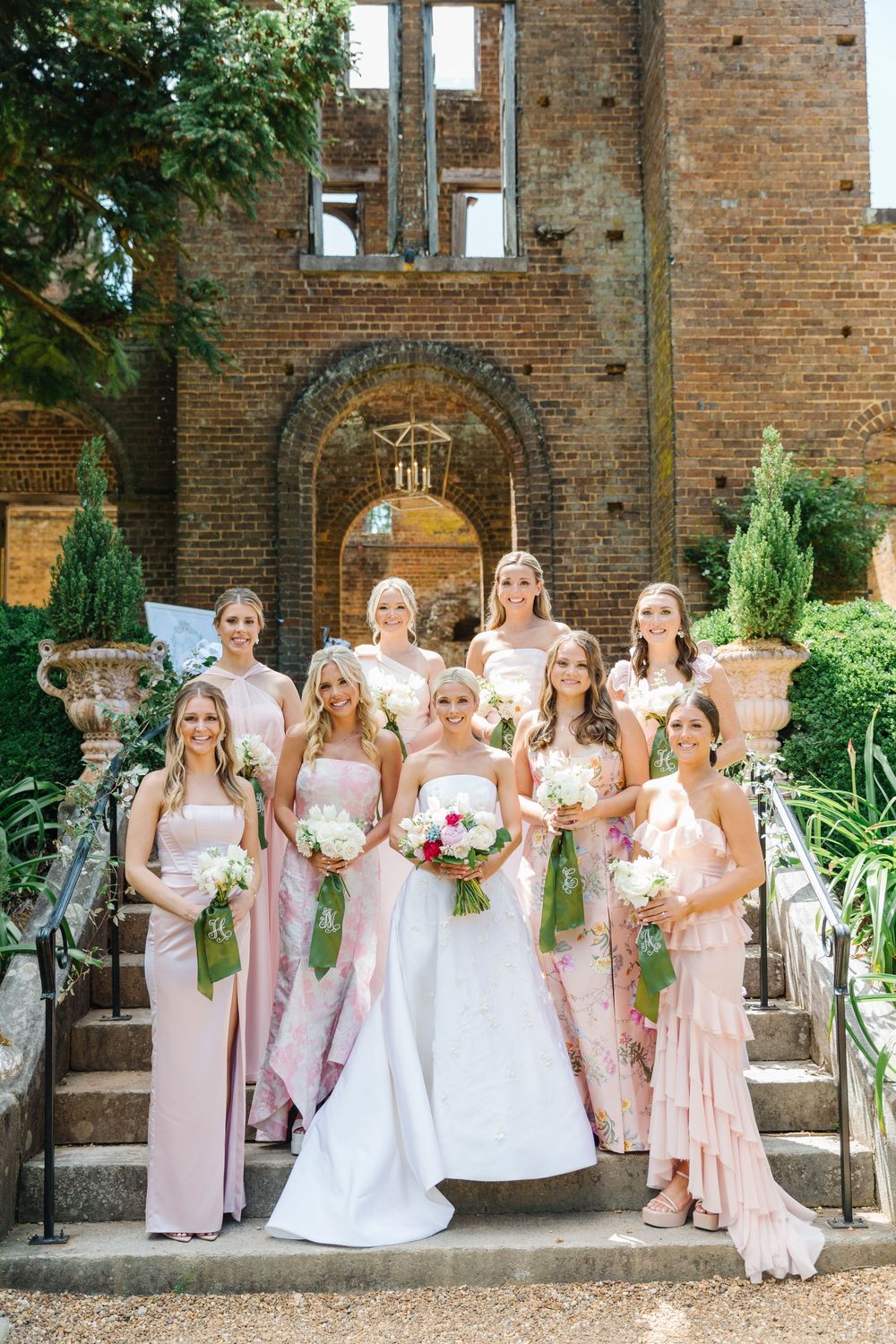 Wedding party poses on brick steps at elegant garden venue with arched architectural details and lush greenery.