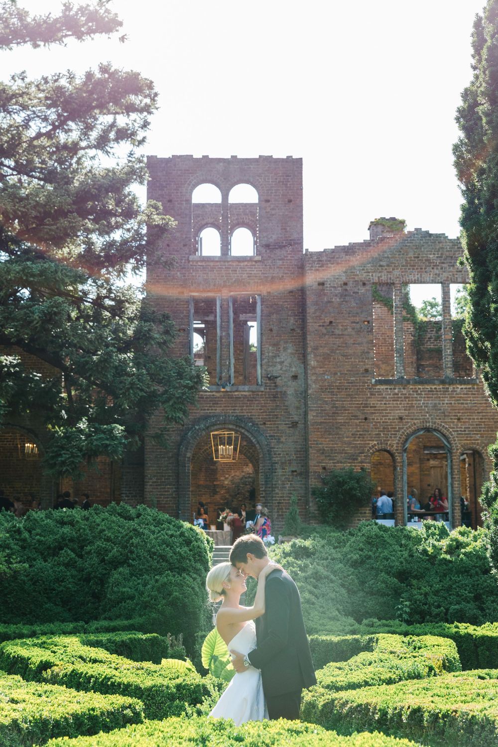 A romantic moment in a garden with historic brick ruins featuring arched windows and lush greenery on a sunny afternoon.
