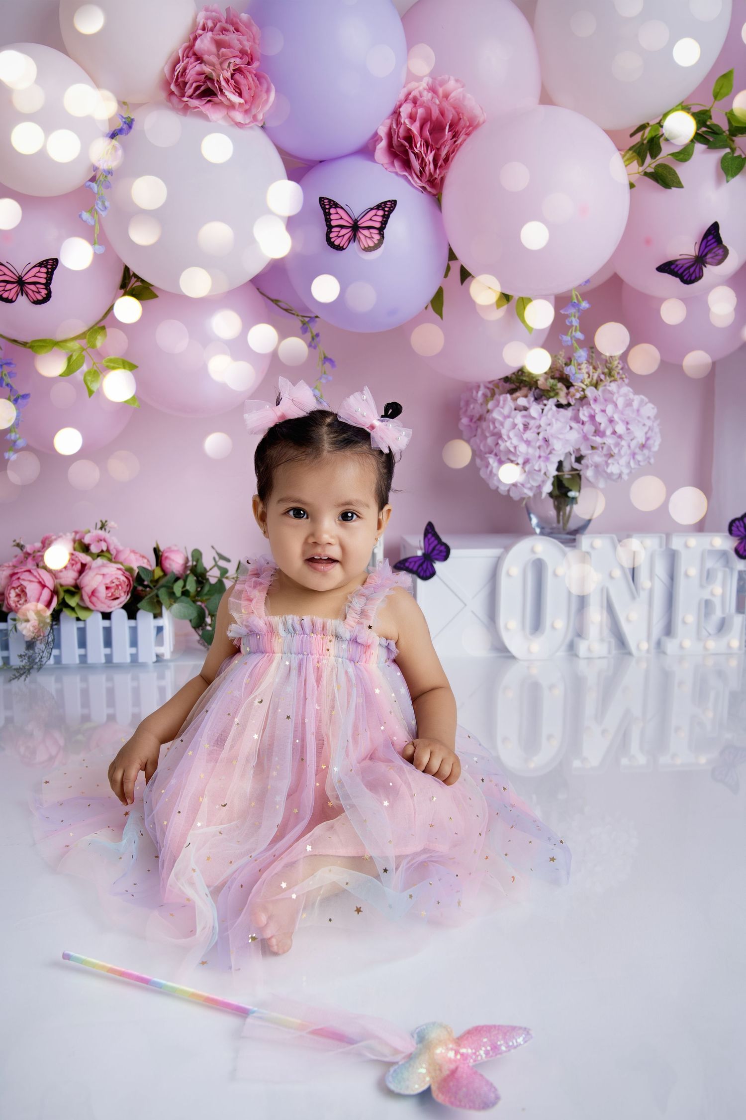 Dreamy pink and purple balloon arch with butterflies and floral accents for birthday photoshoot.