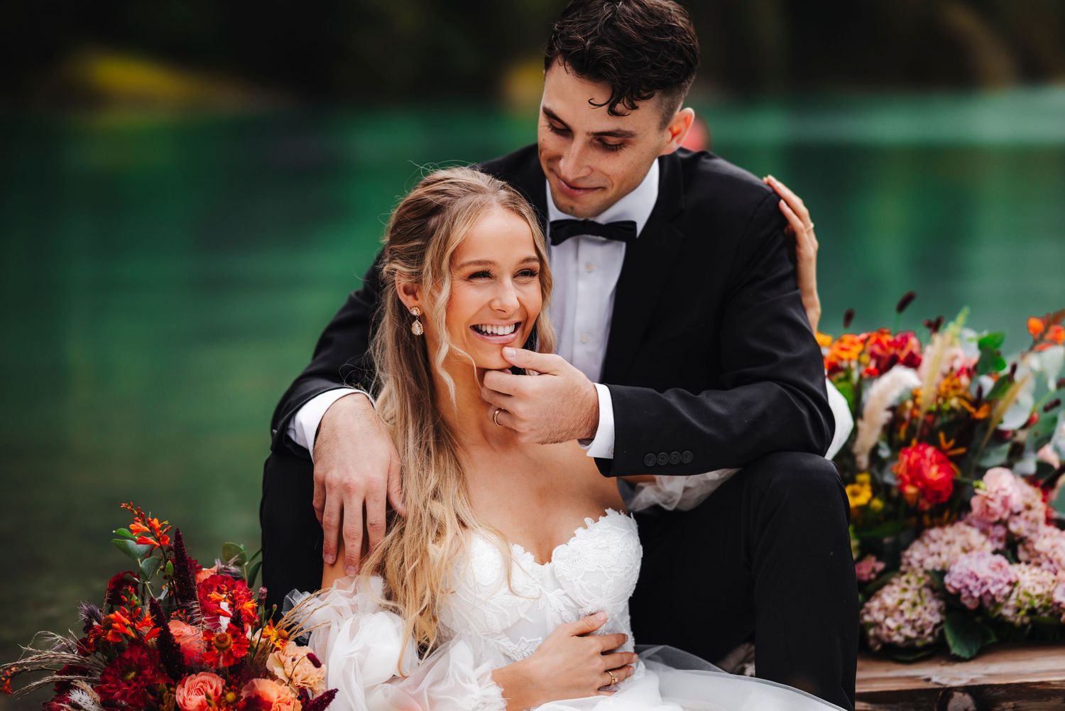 A joyful newlywed couple shares a candid moment during their wedding reception next to vibrant floral arrangements.