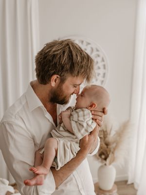 A tender moment captured in a bright white room showing a parent holding and kissing their baby in multiple poses.