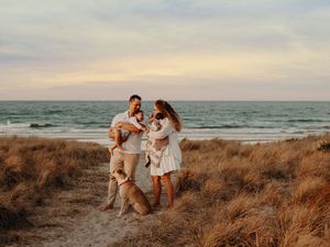 Family playing and laughing together on sand dunes during golden hour at beach.