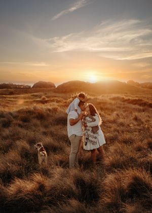 Couple embraces with their dog during golden hour photoshoot in scenic coastal dunes.