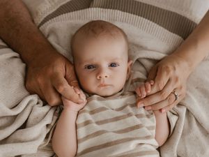 Close-up view of tiny baby hands reaching up against a soft beige background.