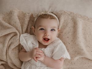 A baby lying on a beige textured blanket shows various expressions while wearing white clothing.