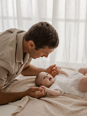 A sweet interaction between parent and infant lying on white bedding in natural light.