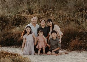 Family sits together on sandy beach during golden hour in coordinated neutral-toned outfits for portrait session.