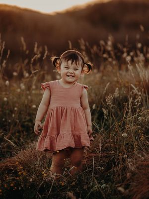 A child in a pink ruffled dress plays in a field at golden hour with a dreamy, moody atmosphere.