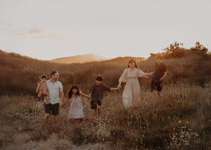 A family walks together through a golden field at sunset during a photo session in the mountains.