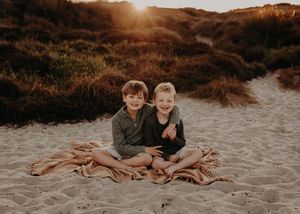 Sun flares over sandy beach during golden hour photoshoot along a winding coastal path. Photographed on Papamoa beach Tauranga