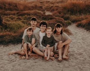 Family together on a sandy beach path during golden hour with warm autumn-toned surroundings in the background. Photographed on Papamoa