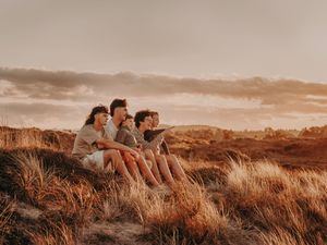 Family sitting together on a hilltop during golden hour overlooking a natural landscape. Photographed on Papamoa beach Tauranga