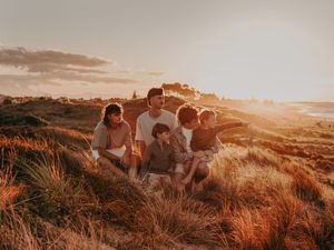 Cousins sits together on grassy hilltop enjoying scenic golden hour sunset over coastal landscape. Photographed on Papamoa beach Tauranga