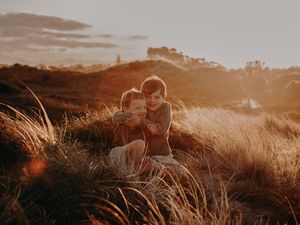 Brothers sit together in tall grass during golden sunset, creating a warm silhouetted moment, Photographed on Papamoa beach Tauranga