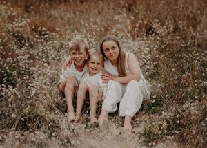 Three people sit together in a rustic field of tall grass during golden hour.