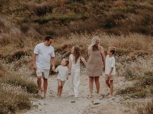 A family walks together holding hands along a dirt path through a golden brown field at sunset.