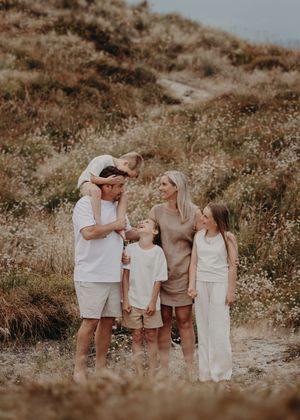 Family wearing neutral colored outfits laughs together during outdoor photo session at golden hour.