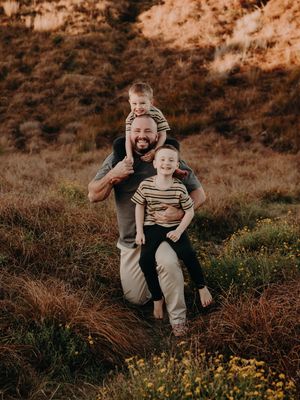 Family enjoying a candid outdoor moment together in a natural setting with golden light and wildflowers at sunset.