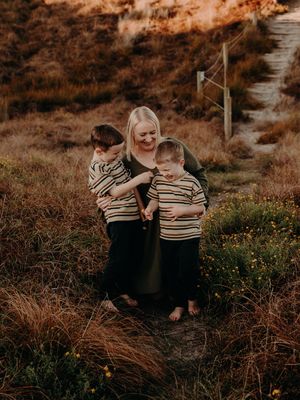 A family in matching striped sweaters embraces while standing on a grassy hill during golden hour.