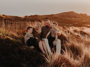 A couple sits together in golden sunlit field of tall grass at sunset, holding each other close.