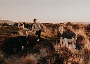 Family playing and relaxing together in scenic golden field during sunset on hillside terrain.