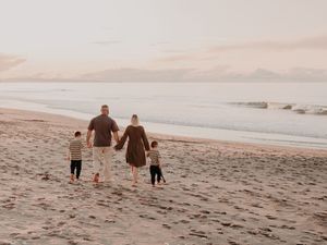 A family walks hand in hand along a serene beach at sunset casting long shadows in the sand.
