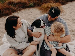 Family snuggling together on sandy beach during casual photo shoot with black and white dog.