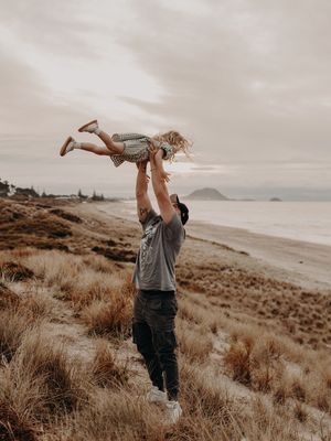 Two people dance and play together on a scenic coastal beach with mountains in the background during golden hour.
