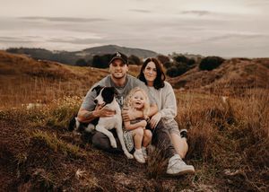 Two people sitting close together in tall autumn grass during golden hour sunset on a hillside.