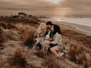 A family sits together on grassy coastal cliffs at sunset overlooking a misty beach shore.