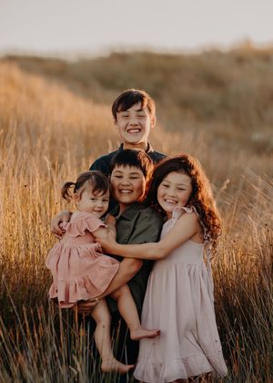 Family embraces in a sun-drenched field of tall grass during golden hour, creating a warm and joyful moment.