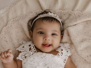 A baby wearing a white lace bonnet lies on cream-colored textured fabric in a collage of close-up shots.