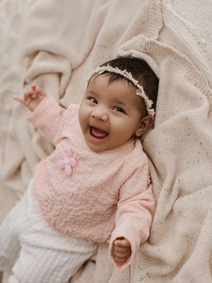 Baby wearing pink sweater lying on cream colored blanket smiling and playing in natural light.