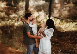 Family shares a joyful moment together in a sunlit forest setting during golden hour. Photographed in a Forest