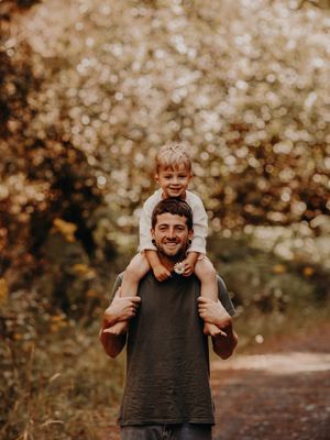 Child riding on shoulders in a park with blurred bokeh lights creating a warm autumn atmosphere. Photographed in a Forest