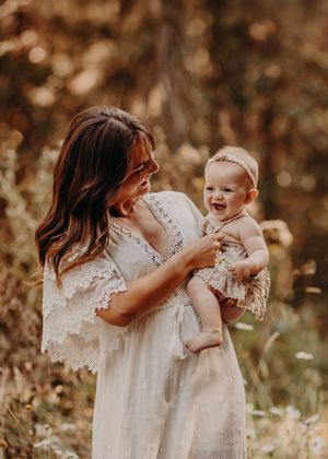 A tender moment captured in warm sepia tones as someone wearing white lace holds and interacts with a baby outdoors.