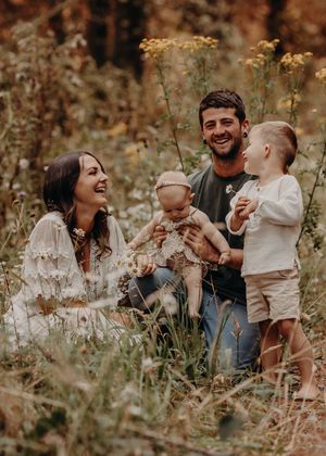 A family shares a candid moment together in a field of tall wildflowers during an autumn photo session. Photographed outdoors in a Forest
