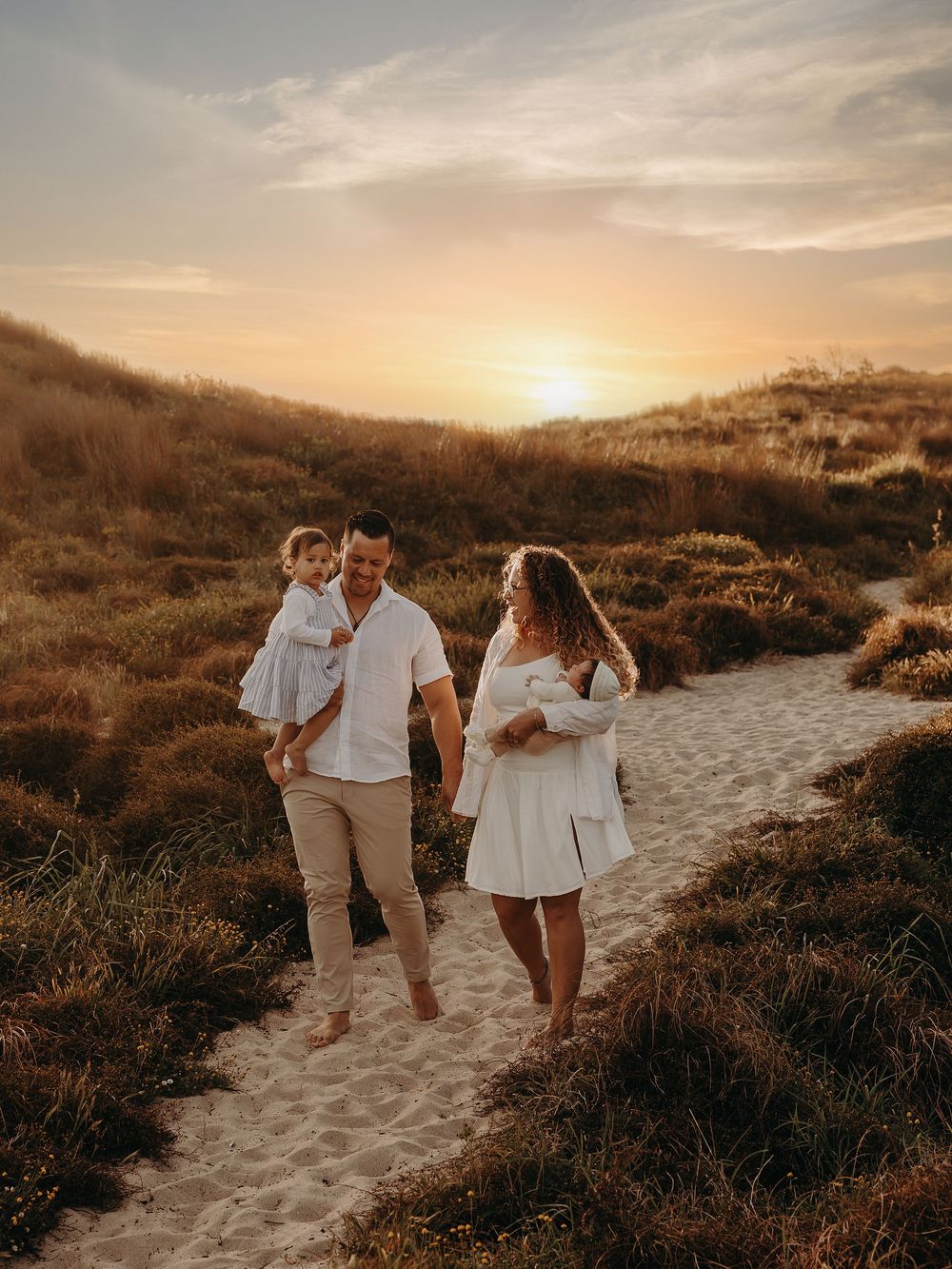 Family walks together on sandy path during sunset beach photoshoot.