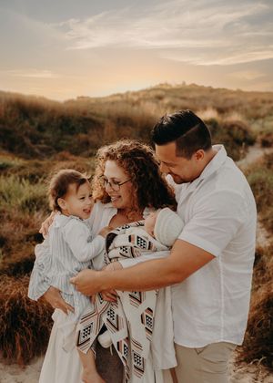 Family sharing intimate playful moment together on beach dunes during sunset.