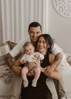 A family lounges together on a white bed, sharing intimate moments in a series of black and white photographs.