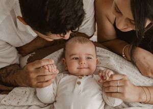 A series of tender moments between a baby and parents lying on white bedding, captured in warm sepia tones.