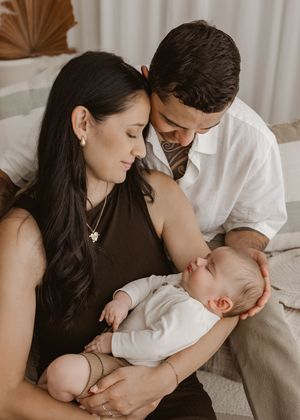 Parents share an intimate moment with their sleeping baby in a warm, natural light setting.
