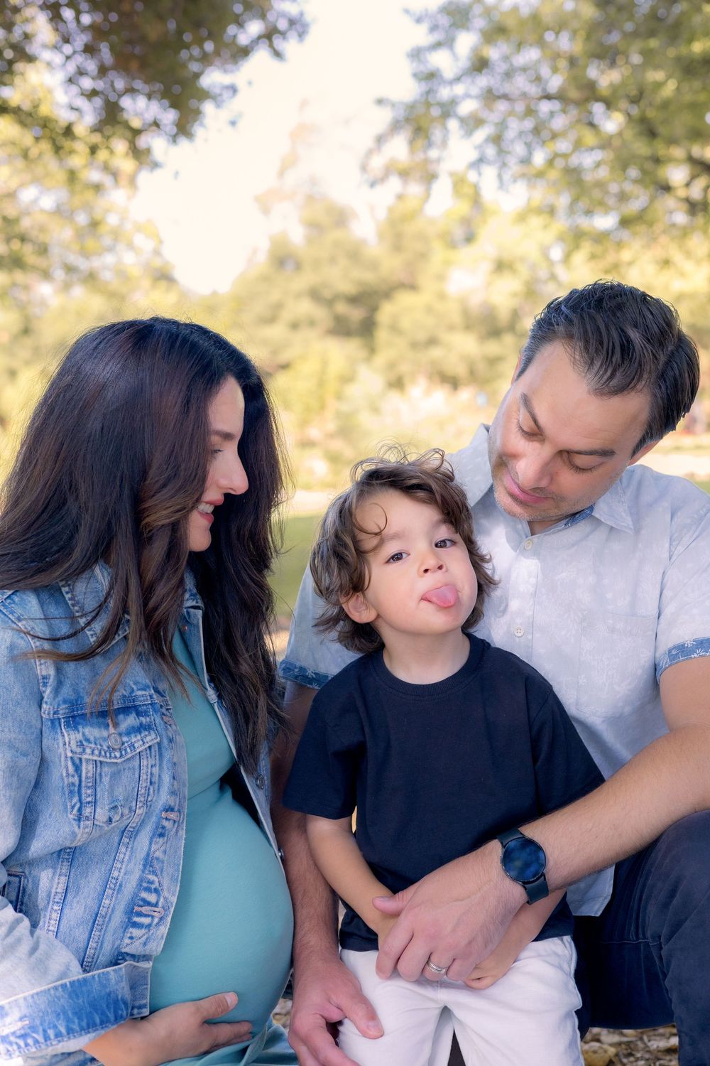 Preschool boy making a funny face while pregnant mom and dad laugh during candid maternity session at Kit Carson Park in Escondido.