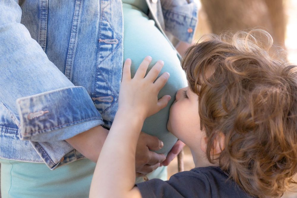 Close-up of little boy kissing his mom’s pregnant belly in intimate moment at maternity session at Kit Carson Park in Escondido, CA.