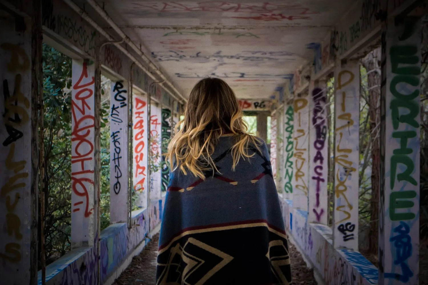 Personne de dos marchant dans un couloir étroit, entièrement couvert de graffitis colorés sur les murs et le plafond.