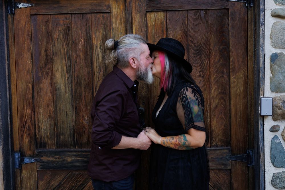 A couple embraces in front of a rustic wooden door with stone walls.