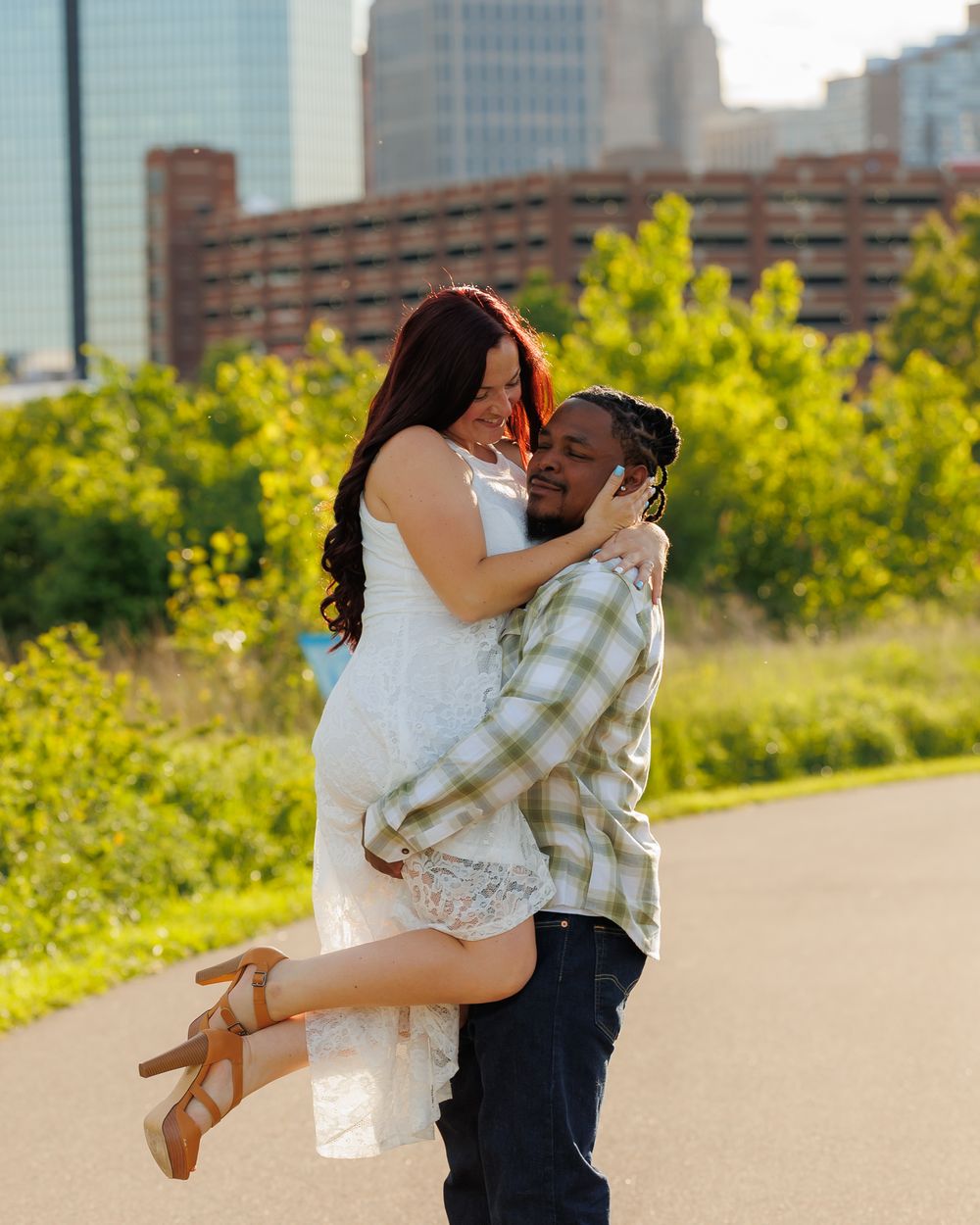 Romantic couple embraces outdoors in late afternoon sunlight with urban buildings in background.