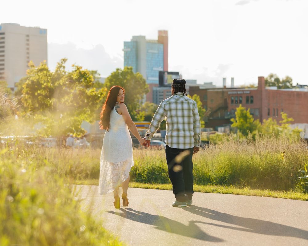 A romantic couple walking together at sunset on a city path with warm golden light streaming around them.