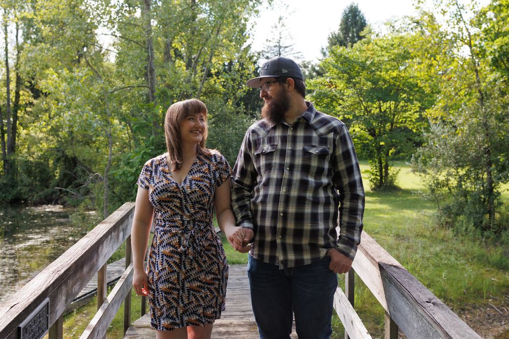A couple walks together and shares drinks while strolling along a wooden boardwalk path through a lush green park.